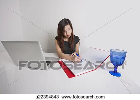Stock Image - Young businesswoman writing on diary at office desk. Fotosearch