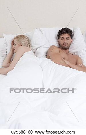 Stock Image - Young couple avoiding each other in bed. Fotosearch
