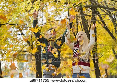 Young couple enjoying falling autumn leaves in park View Large Photo Image Stock Photography - Young couple enjoying falling autumn leaves in park. Fotosearch