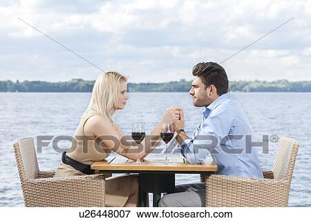 Young couple holding hands while looking at each other at outdoor restaurant by lake View Large Photo Image Stock Photo - Young couple holding hands while looking at each other at outdoor restaurant by lake. Fotosearch