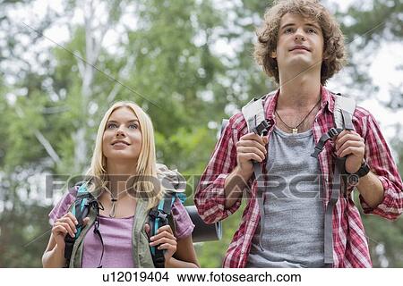Picture - Young couple looking away while hiking in forest. Fotosearch