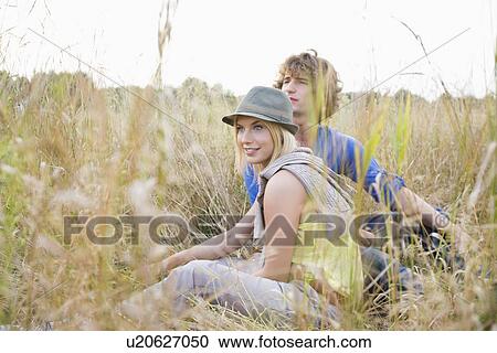 Stock Image - Young couple looking away while relaxing in field. Fotosearch