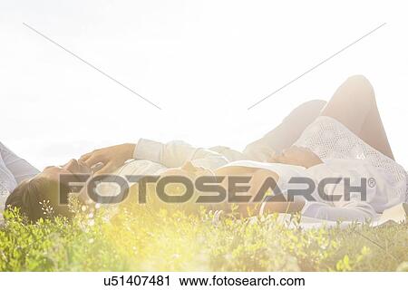 Stock Image - Young couple lying on grass against clear sky. Fotosearch
