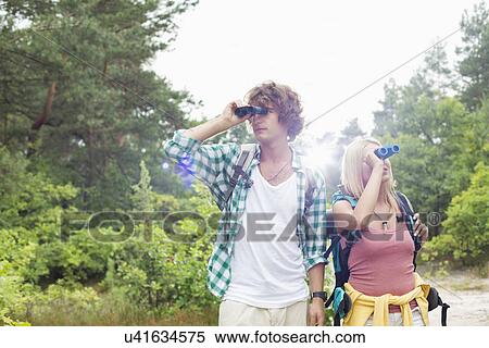Young couple using binoculars while hiking in forest View Large Photo Image Stock Photography - Young couple using binoculars while hiking in forest. Fotosearch