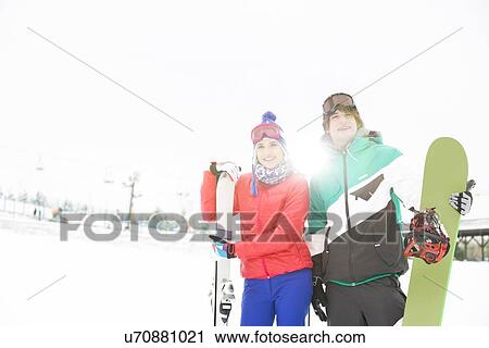 Stock Image - Young couple with snowboard and skis in snow. Fotosearch