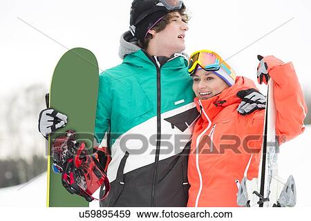 Stock Photo - Young couple with snowboard and skis in snow. Fotosearch
