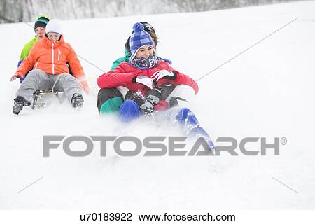 Stock Image - Young couples enjoying sled ride on snow covered slope. Fotosearch
