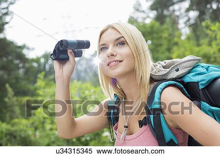 Stock Photography - Young female hiker using binoculars in forest. Fotosearch