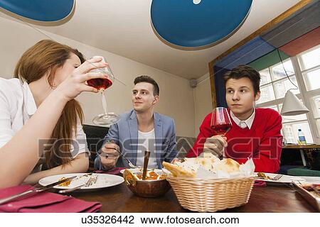 Stock Image - Young friends having meal at restaurant. Fotosearch