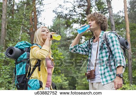 Stock Image - Young hiking couple drinking energy drinks in forest. Fotosearch