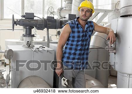 Stock Photo - Young labor holding wrench while leaning on industrial machine. Fotosearch