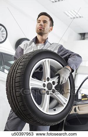 Young maintenance engineer carrying tire in automobile store View Large Photo Image Stock Image - Young maintenance engineer carrying tire in automobile store. Fotosearch