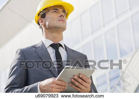 Stock Image - Young male architect holding tablet PC against building. Fotosearch