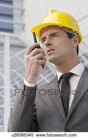 Young male architect talking on walkie-talkie against building View Large Photo Image Stock Photography - Young male architect talking on walkie-talkie against building. Fotosearch