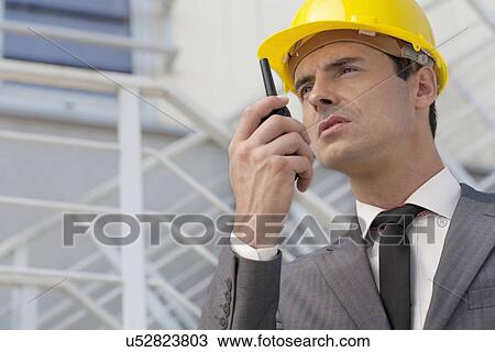 Stock Image - Young male architect talking on two-way radio against building. Fotosearch