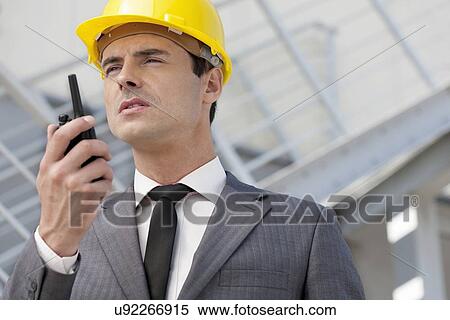 Young male architect talking on two-way radio outdoors View Large Photo Image Stock Photography - Young male architect talking on two-way radio outdoors. Fotosearch