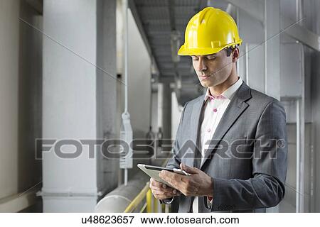 Stock Photo - Young male architect using tablet computer in industry. Fotosearch