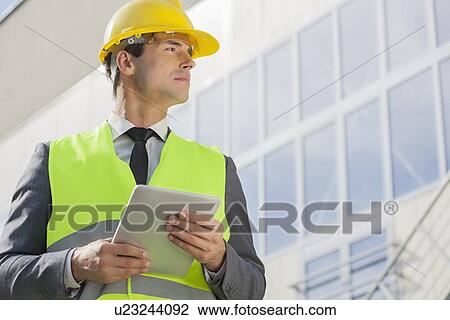Stock Image - Young male architect with digital tablet looking away outside building. Fotosearch