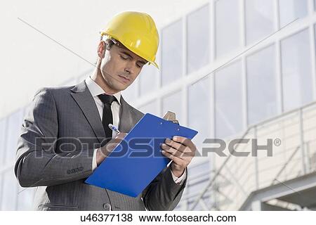 Young male architect writing on clipboard against office building View Large Photo Image Stock Photo - Young male architect writing on clipboard against office building. Fotosearch