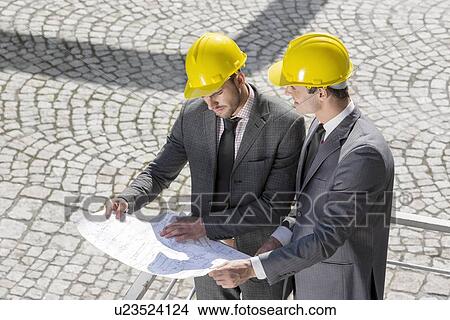 Young male architects analyzing blueprint at construction site View Large Photo Image Picture - Young male architects analyzing blueprint at construction site. Fotosearch