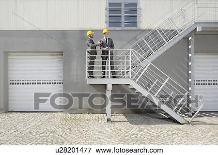 Young male architects with clipboard discussing on stairway View Large Photo Image Stock Photo - Young male architects with clipboard discussing on stairway. Fotosearch