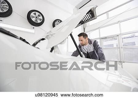 Stock Photography - Young male automobile mechanic examining car engine in repair shop. Fotosearch
