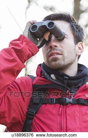 Stock Photograph - Young male backpacker using binoculars in forest. Fotosearch