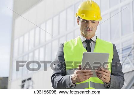 Young male engineer in reflector-vest and hardhat using digital tablet outside industry View Large Photo Image Stock Photo - Young male engineer in reflector-vest and hardhat using digital tablet outside industry. Fotosearch