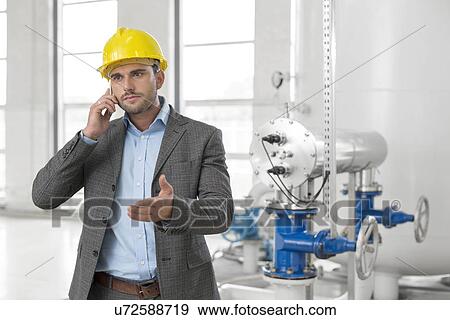 Stock Photo - Young male engineer using cell phone in industry. Fotosearch