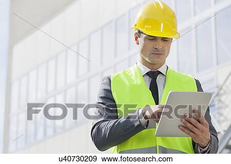 Stock Photo - Young male engineer using digital tablet outside industry. Fotosearch