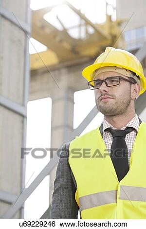 Young male engineer wearing hard hat looking away at construction site View Large Photo Image Stock Photograph - Young male engineer wearing hard hat looking away at construction site. Fotosearch