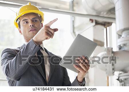 Young male engineer with digital tablet pointing away in industry View Large Photo Image Stock Image - Young male engineer with digital tablet pointing away in industry. Fotosearch