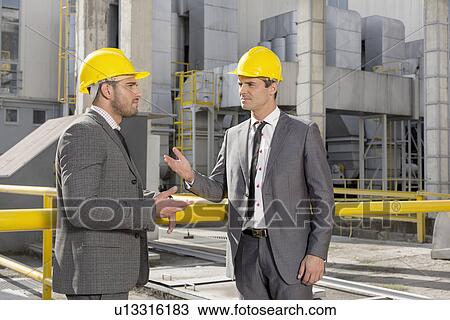 Stock Image - Young male engineers discussing at construction site. Fotosearch