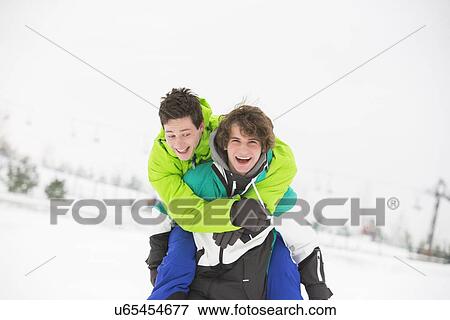 Young male friends enjoying piggyback ride in snow View Large Photo Image Stock Photo - Young male friends enjoying piggyback ride in snow. Fotosearch