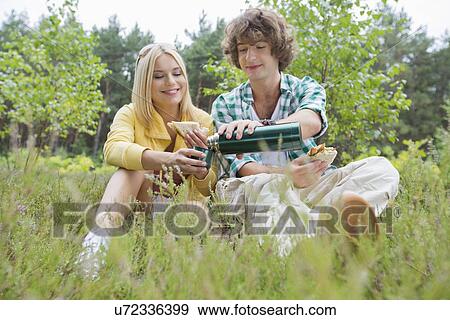 Young male hiker pouring coffee for woman while relaxing in field View Large Photo Image Stock Photo - Young male hiker pouring coffee for woman while relaxing in field. Fotosearch