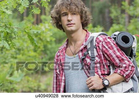 Stock Photo - Young male hiker with backpack looking away in forest. Fotosearch