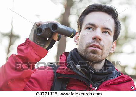 Stock Photograph - Young male hiker with binoculars in forest. Fotosearch