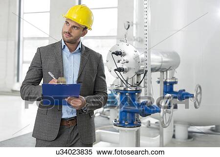 Young male inspector writing on clipboard while looking away in industry View Large Photo Image Stock Photography - Young male inspector writing on clipboard while looking away in industry. Fotosearch