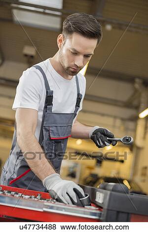 Stock Photo - Young male maintenance engineer arranging tools in drawer at car workshop. Fotosearch