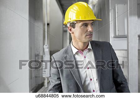 Young male supervisor wearing hard hat looking away in industry View Large Photo Image Stock Photography - Young male supervisor wearing hard hat looking away in industry. Fotosearch