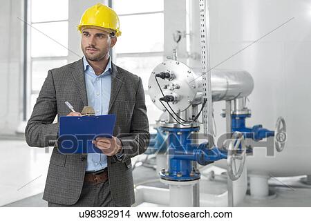 Picture - Young male supervisor writing on clipboard in industry. Fotosearch