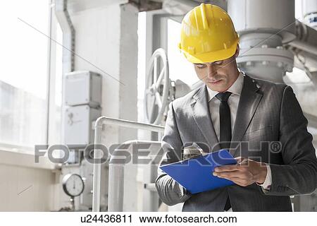 Stock Image - Young male supervisor writing on clipboard in industry. Fotosearch