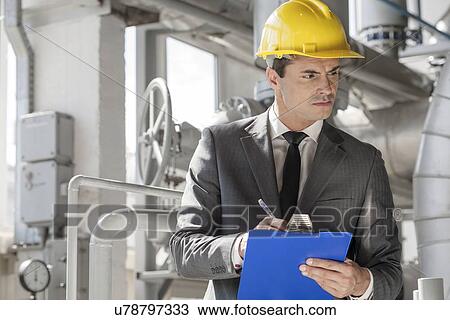 Stock Image - Young male supervisor writing on clipboard in industry. Fotosearch
