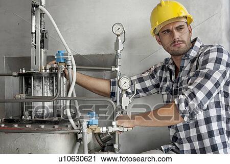 Stock Image - Young male worker examining machine in industry. Fotosearch
