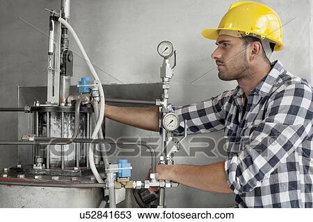 Stock Image - Young male worker examining machine in industry. Fotosearch