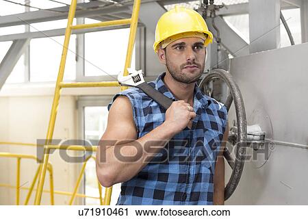 Young male worker with wrench leaning on large industrial valve View Large Photo Image Stock Image - Young male worker with wrench leaning on large industrial valve. Fotosearch