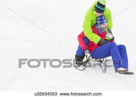 Young man embracing woman on sled in snow View Large Photo Image Stock Image - Young man embracing woman on sled in snow. Fotosearch
