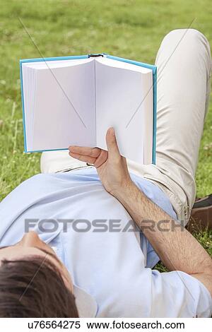 Young man holding book while lying in park View Large Photo Image Stock Photography - Young man holding book while lying in park. Fotosearch