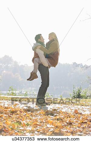 Young man lifting woman in park during autumn View Large Photo Image Stock Image - Young man lifting woman in park during autumn. Fotosearch