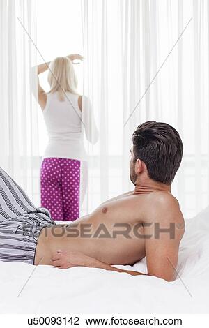 Young man looking at woman standing by window in hotel room View Large Photo Image Stock Image - Young man looking at woman standing by window in hotel room. Fotosearch